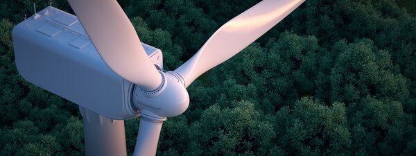 Bild vergr&ouml;&szlig;ern: Close up of wind turbine with lush forest in the background.