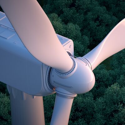 Close up of wind turbine with lush forest in the background. 